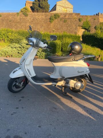 White scooter on a path with grass and a wall